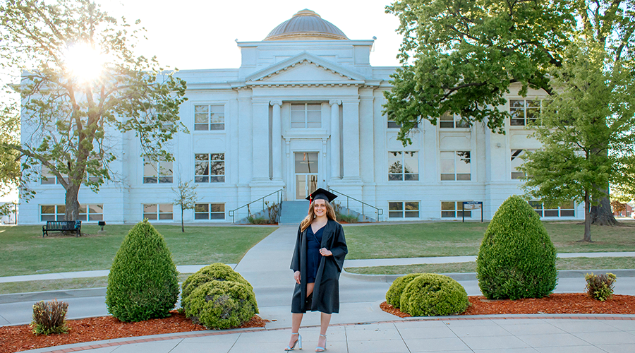 graduate in front of white building with gold dome