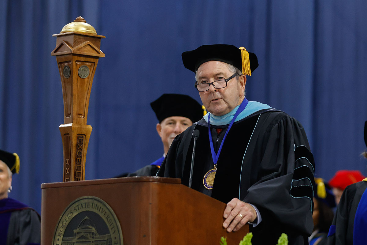 man in cap and gown speaking at podium