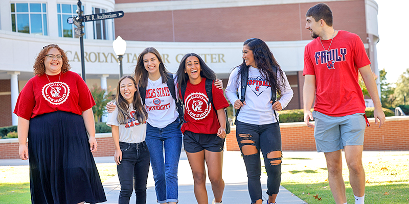 Group of students walking across campus talking and laughing.