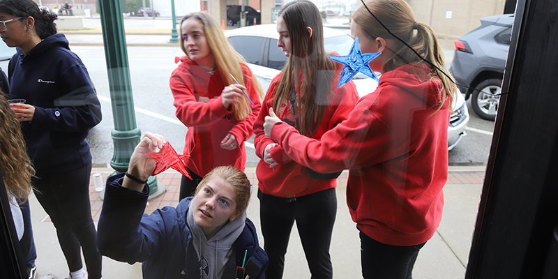 Students painting windows of business for homecoming.