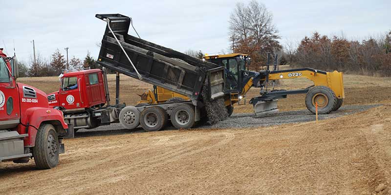 Work trucks putting gravel down for a parking lot.