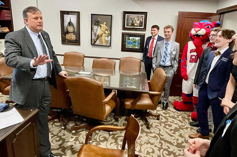 students and mascot listening to man speaking in office