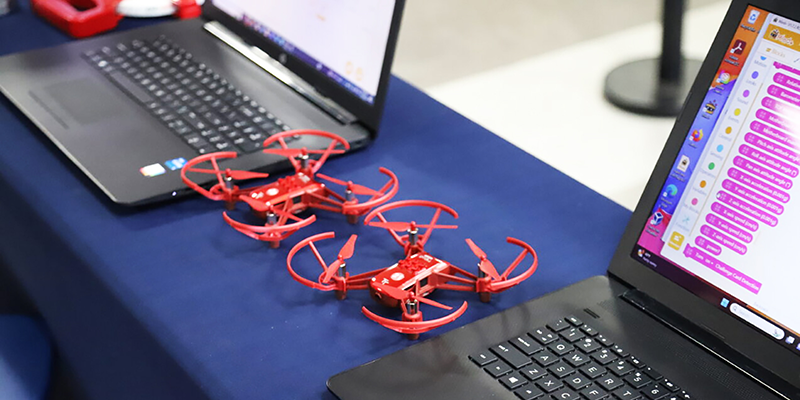 2 red drones next to laptops with programming on screen.