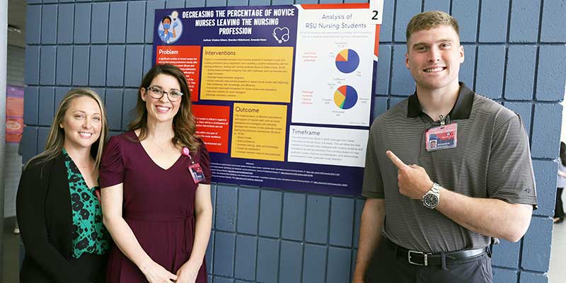 Two girls and a guy pointing at poster.