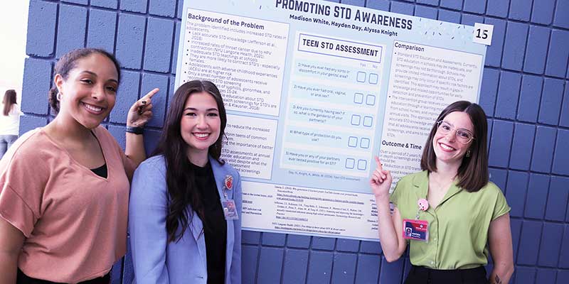 Three girls pointing at a poster.