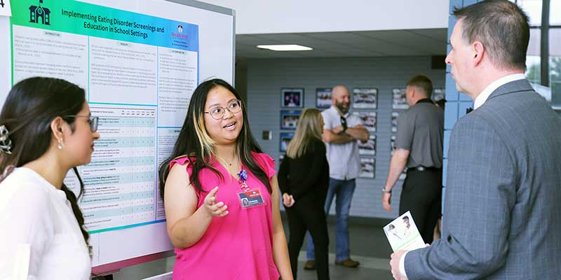 Two girls explaining their poster presentation to a man.