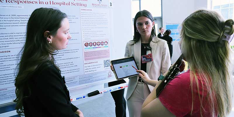 Two girls explaining their poster presentation to another girl.