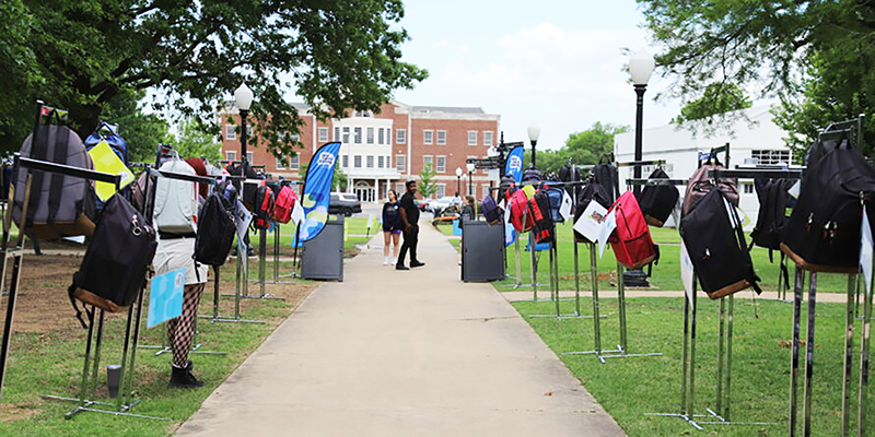 Rows of backpacks hanging on racks along sidewalk.