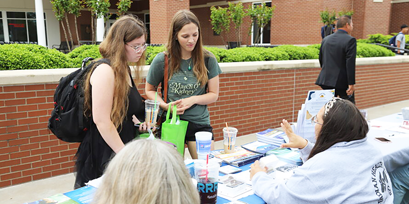 Girls speaking to someone at a table.