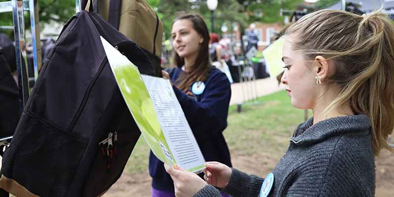 Girl reading a note hanging from a backpack.