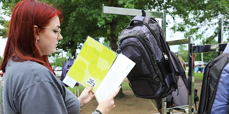 Girl reading a note hanging from a backpack.