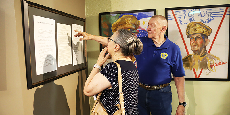 Man pointing to exhibit on the wall with woman looking on in the Oklahoma Military Academy Museum.