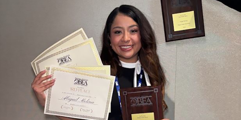 A girl smiles while holding awards.
