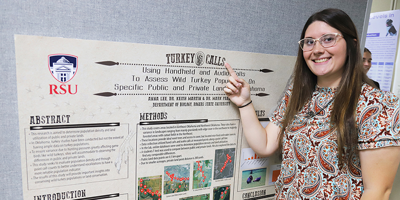 A smiling student points to her research poster.