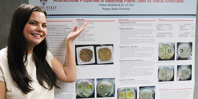 A smiling student points to her research poster.