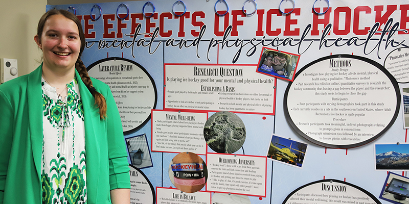 A female student smiles in front of her research poster.