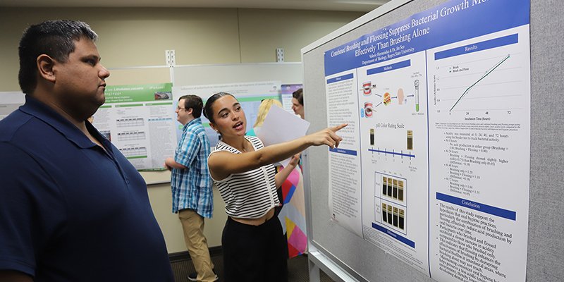 A female student presents her poster project to a male profeessor.
