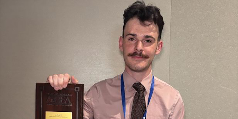 A male RSU student holds an award.