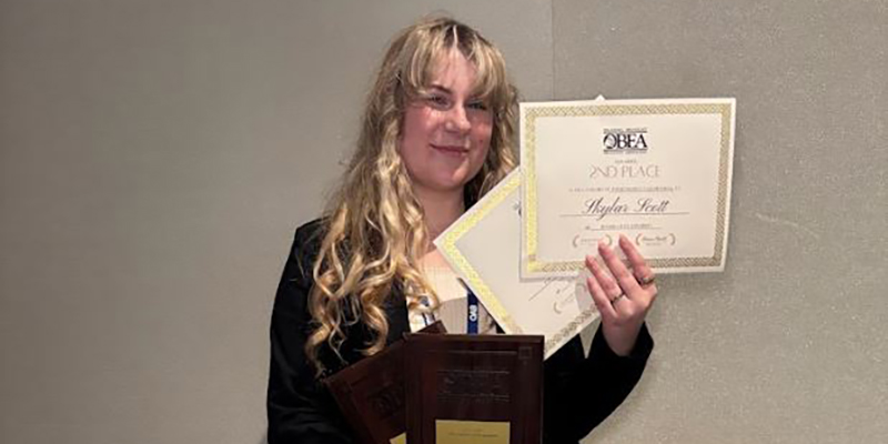 A girl smiles while holding awards.