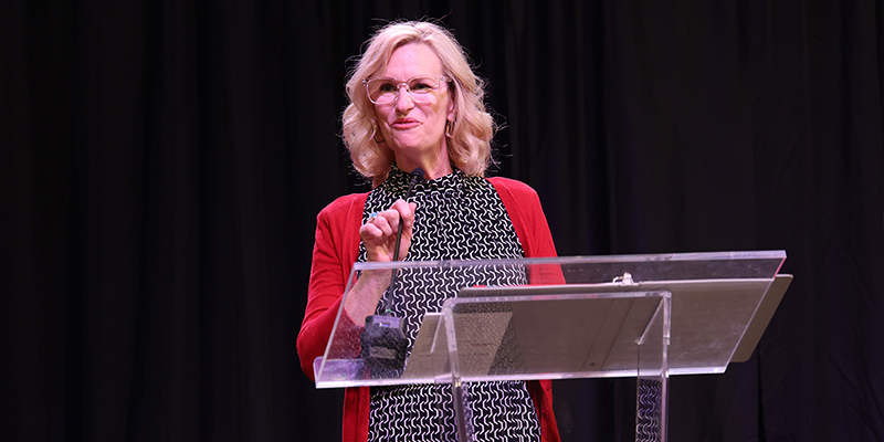 A smiling woman speaks into a microphone at a podium