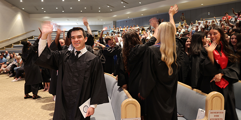 Students in graduation robes wave to the audience.