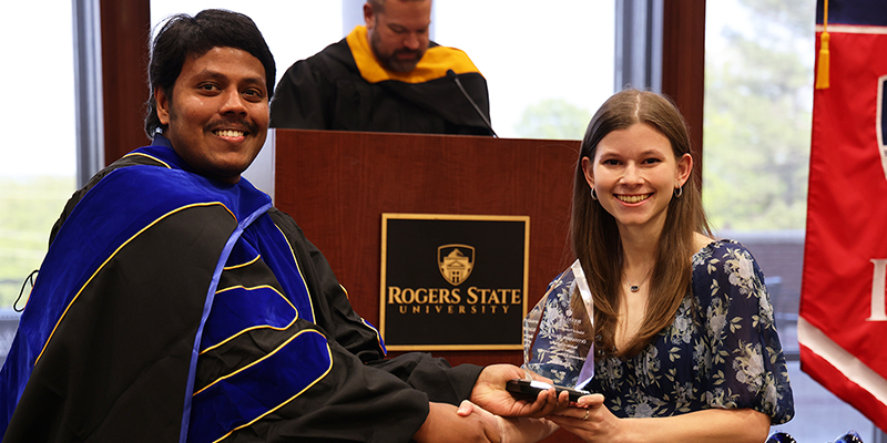 A smiling man shakes the hand of a smiling woman while presenting her with an award.
