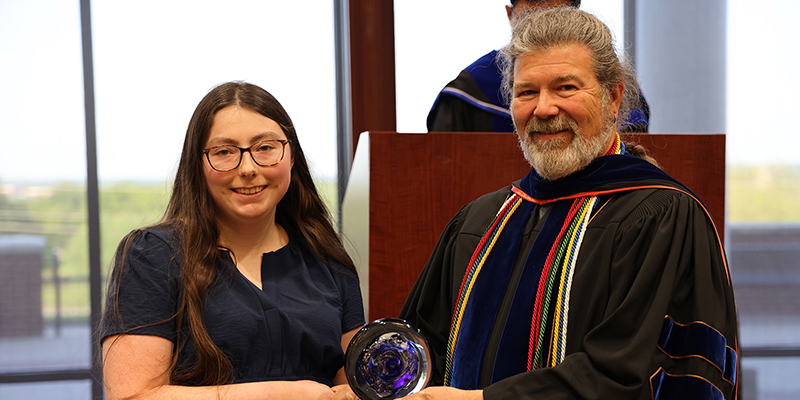 A female student receives an award from a male professor.