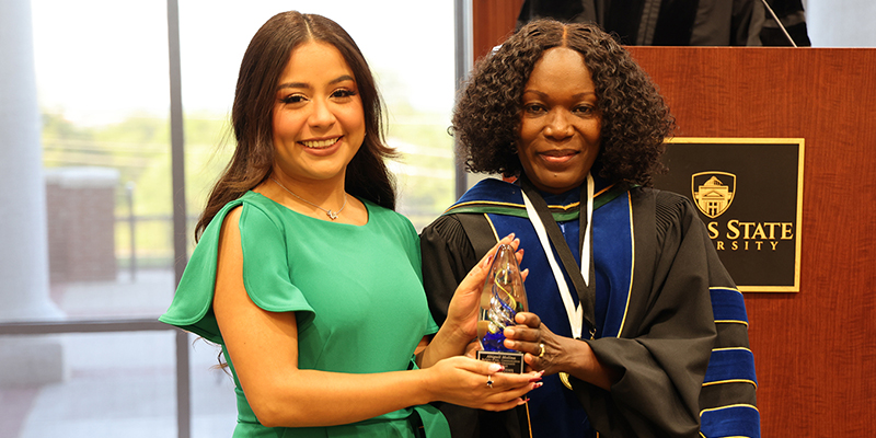 A female student receives an award from a female professor.