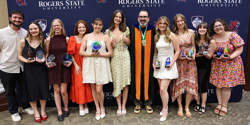 A large group of students holding their awards while posing with a professor.