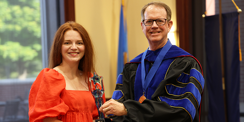 A smiling professor to the right present an award to a female student on the left.