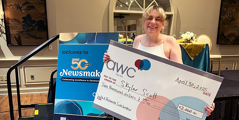 A smiling young woman holds a giant cardboard scholarship check