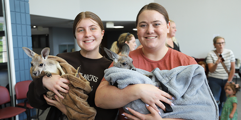 Two smiling girls each hold a baby kangaroo