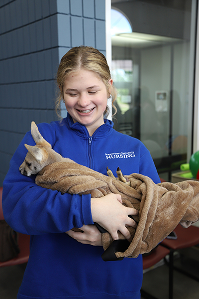 A smiling girl holds a baby kangaroo