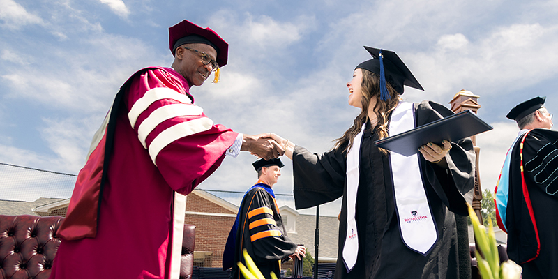 The male commencement speaker shakes the hand of a female graduate