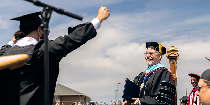 A happy graduate raises his hand in celebration as the university president smiles