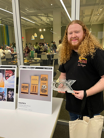 A man stands posing with an award and his artwork.