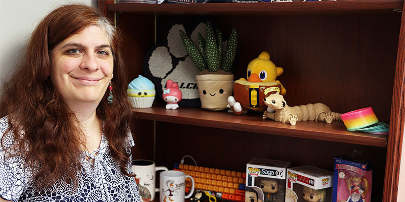 A smiling woman stands next to a shelf of collectibles