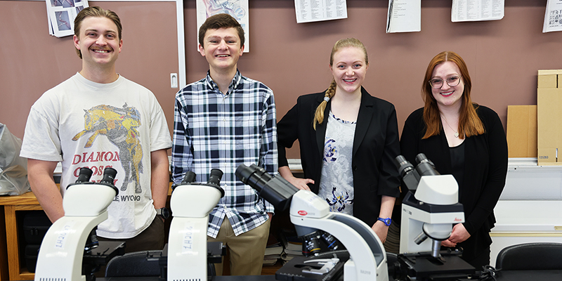 Four smiling students in a science lab.
