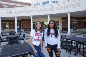 Two students on deck of the Dr. Carolyn Tayler Center near some tables and looking thrilled