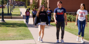 Five students smiling and walking down a sidewalk.